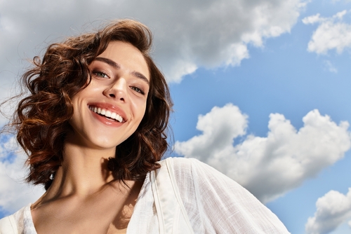 A,Young,Woman,With,Wavy,Brown,Hair,Smiles,Outdoors,On